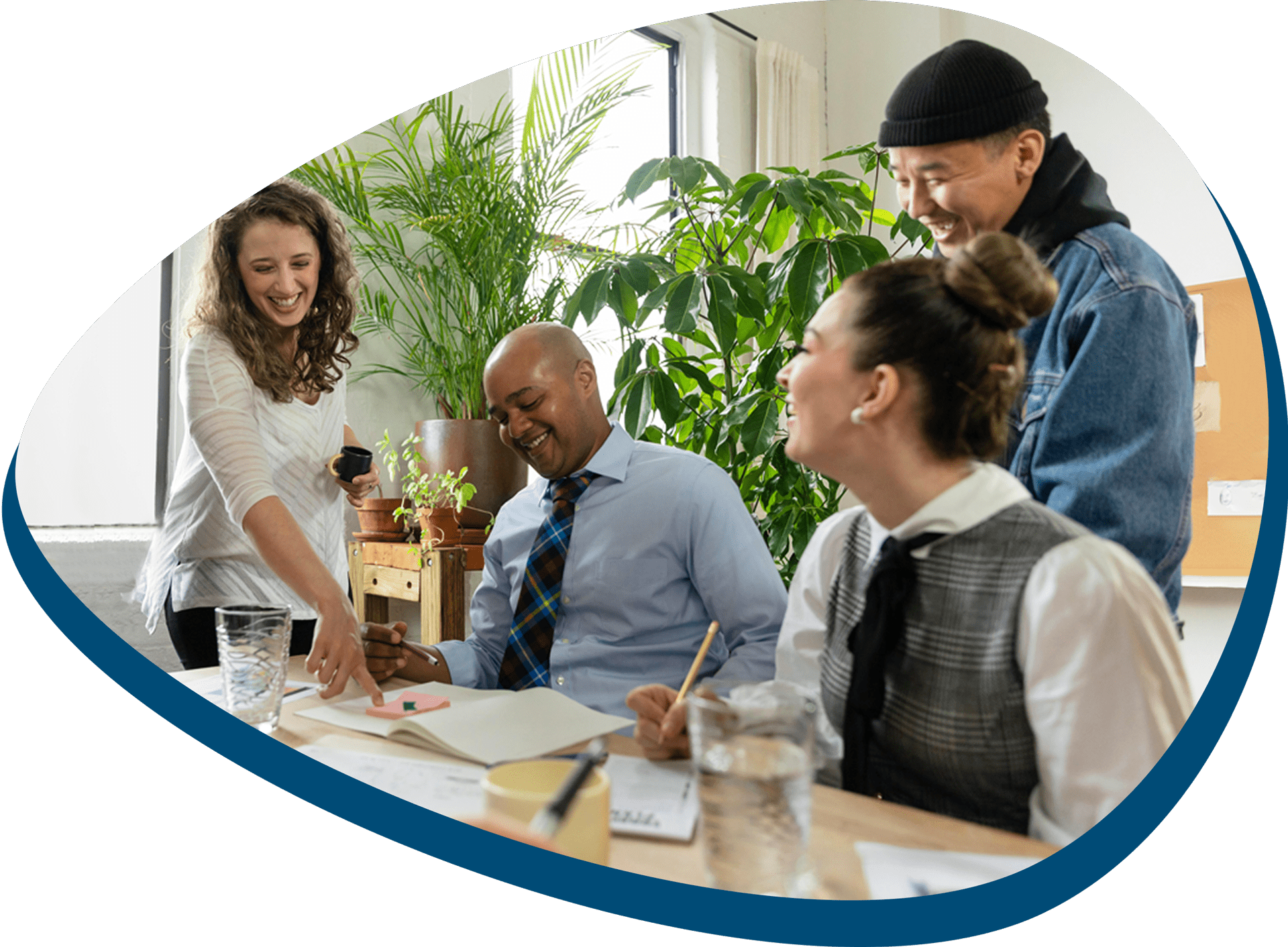 Vier Menschen arbeiten gemeinsam lachend an einem Schreibtisch im Büro.